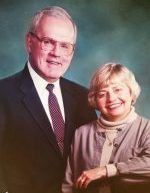Older man and woman smiling, posed together. Man in suit, woman in sweater.