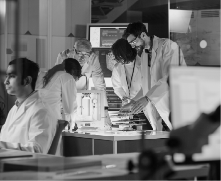 Group of scientists in lab coats examining equipment in a research laboratory.