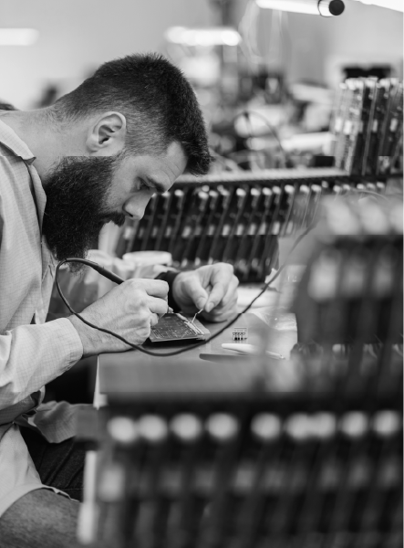 Man soldering electronics, seated at a workbench in a factory setting, focused.