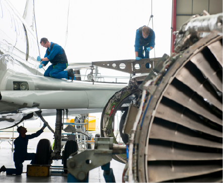 Aircraft mechanics working on a plane in a hangar, with an exposed engine in the foreground.