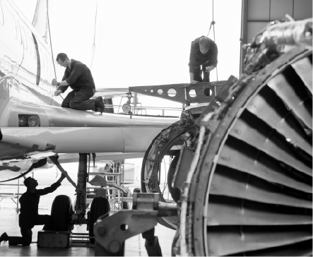 Mechanics work on an airplane wing and engine in a hangar.