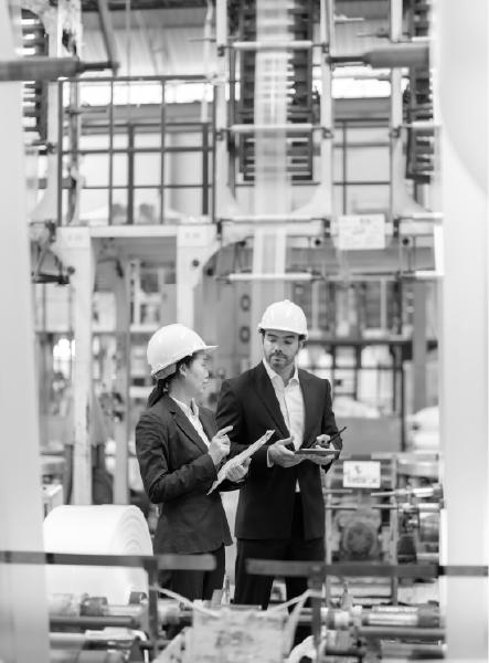 Two people in hard hats, looking at equipment in a factory.
