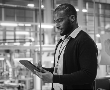 Man in a cardigan looks at a tablet in an office setting, possibly managing operations.