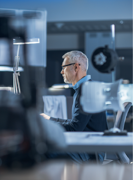 Man with glasses works at a computer in a modern, bluish-lit workshop.