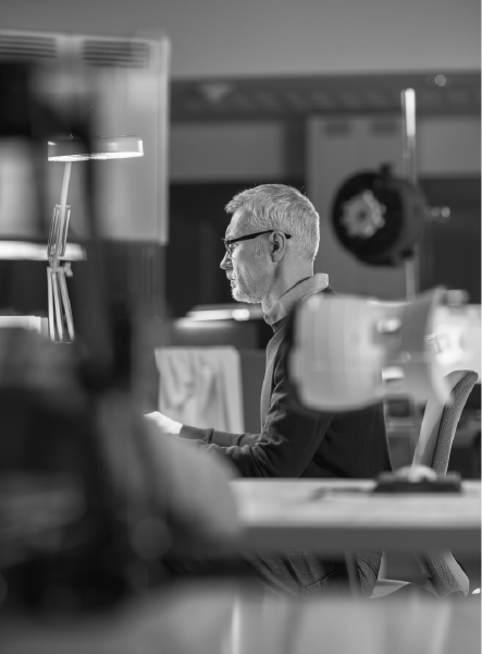 Man with glasses, side profile, working at a desk. Office setting, in black and white.