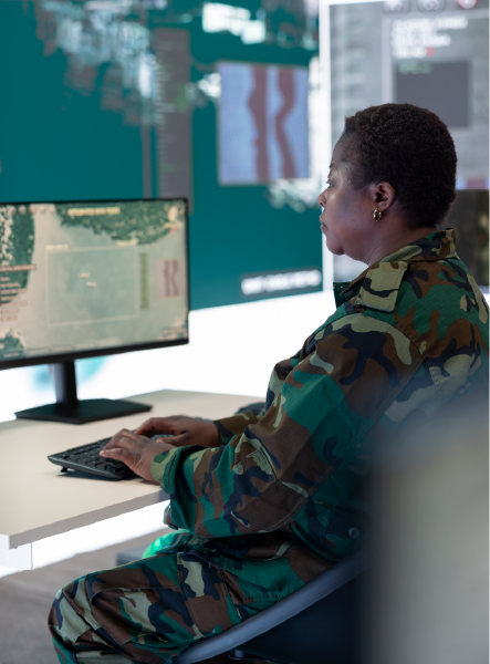 Person in camouflage uniform at computer, looking at screens displaying data in a control room.