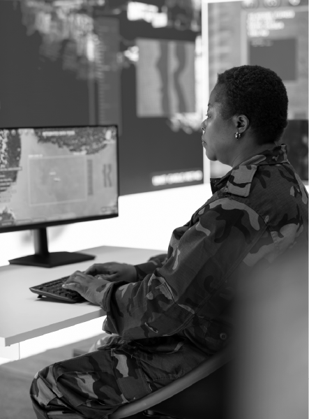 Woman in camouflage uniform at computer, analyzing data in control room.