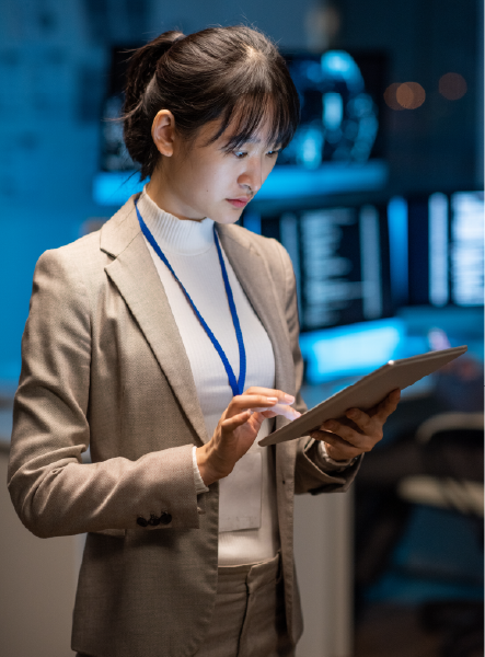 Woman in suit using tablet in a tech room, with computer screens in the background.