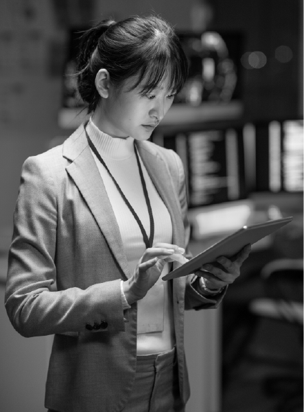 Woman in a suit uses a tablet in a tech-filled room, with a focused expression.