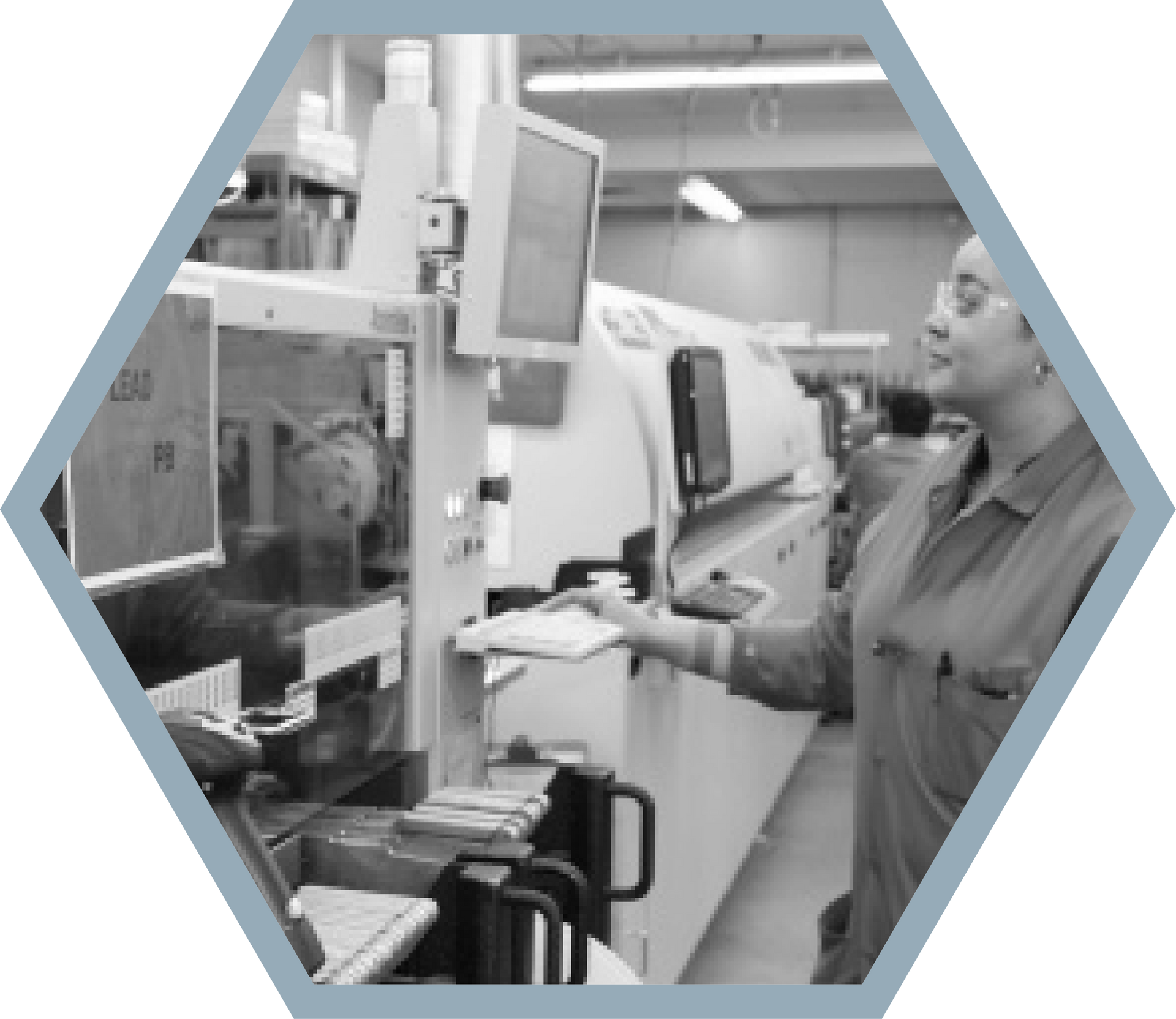 A worker in a factory setting using a computer near machinery.