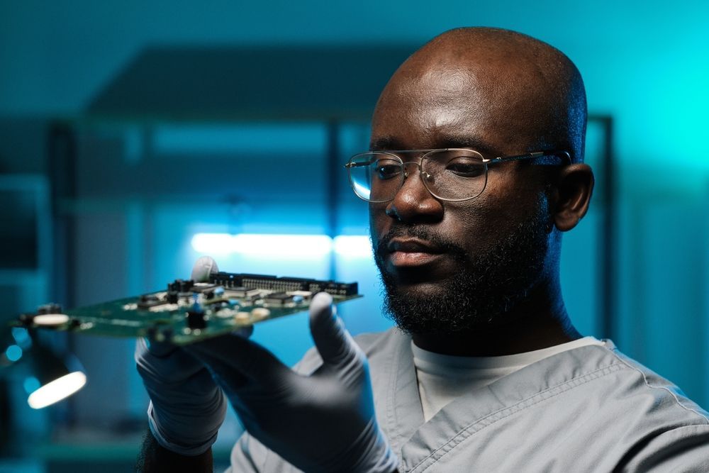 A person wearing gloves examining a circuit board in a lab setting.
