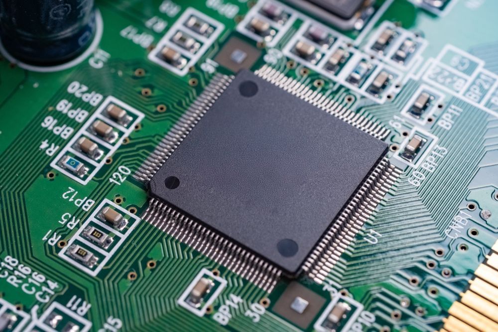 Close-up of a green circuit board with a black microchip and surrounding electronic components