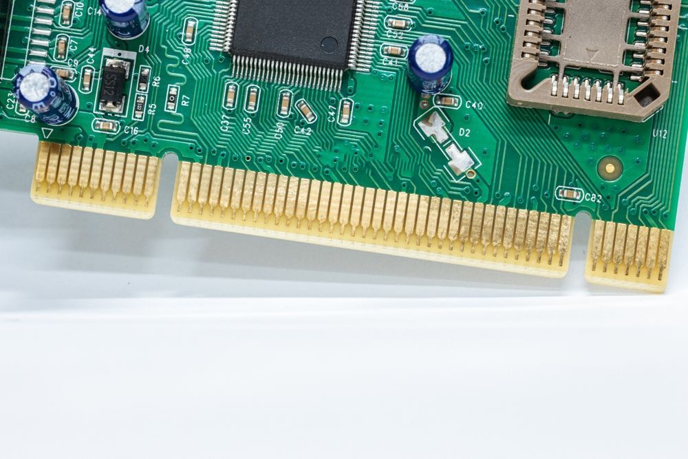 Close-up of a green circuit board with gold connectors and electronic components on a white surface.