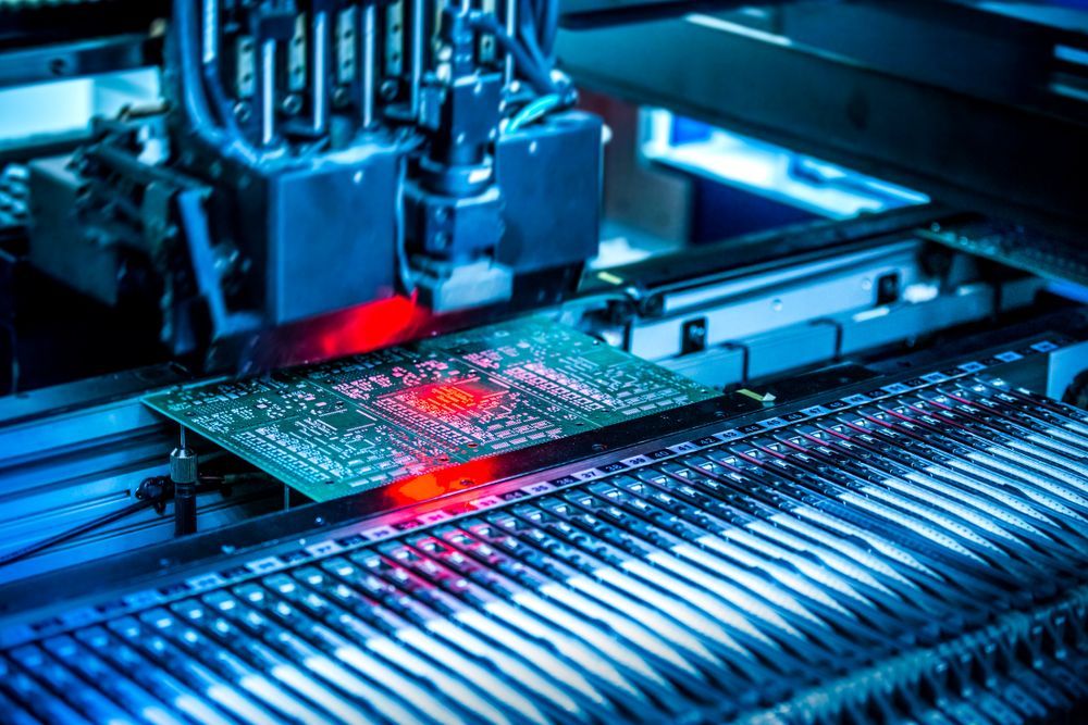 Automated machine assembling circuit board with red light. Industrial setting, blue hues.