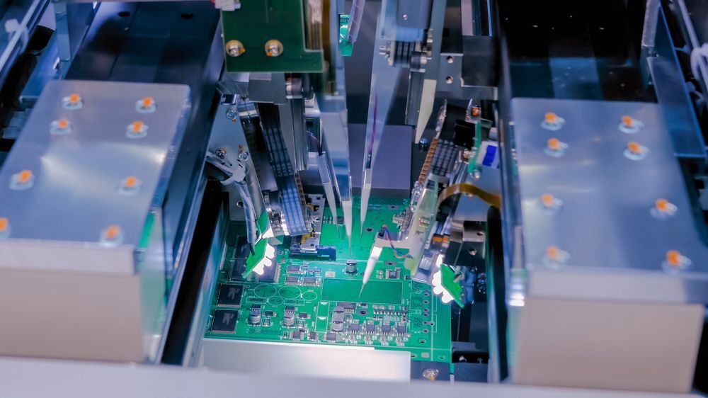 Automated circuit board assembly machine placing electronic components on a green circuit board.