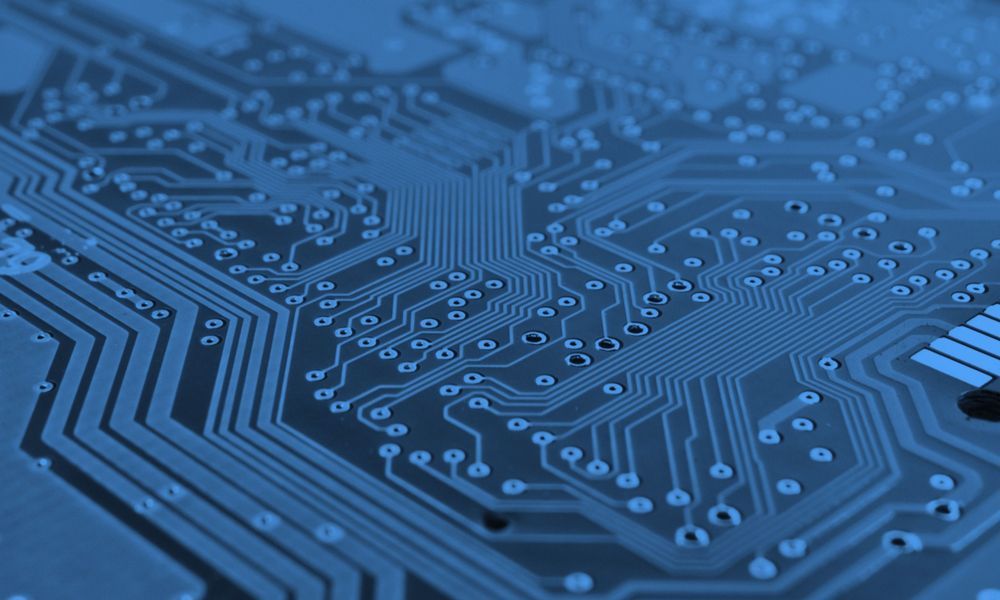 Blue close-up of a circuit board with intricate pathways and components.