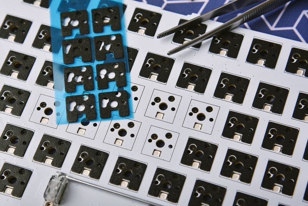 Close-up of a keyboard PCB with switch stabilizers and a sheet of switch pads.