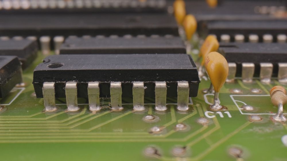 Close-up of a green circuit board with black integrated circuits and yellow capacitors soldered on.