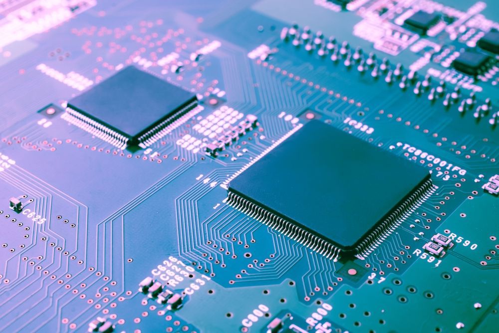 Close-up of a circuit board with two black square chips, intricate lines, and various electronic components.