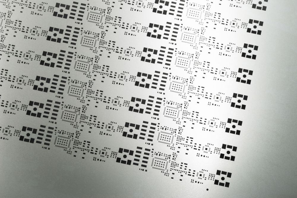 Sheet with many small, repeating patterns of black geometric shapes on a silver surface.