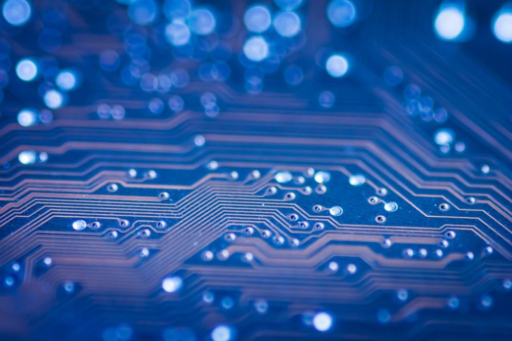 Close-up of a blue circuit board with interconnected lines and points, illuminated with soft blue bokeh.