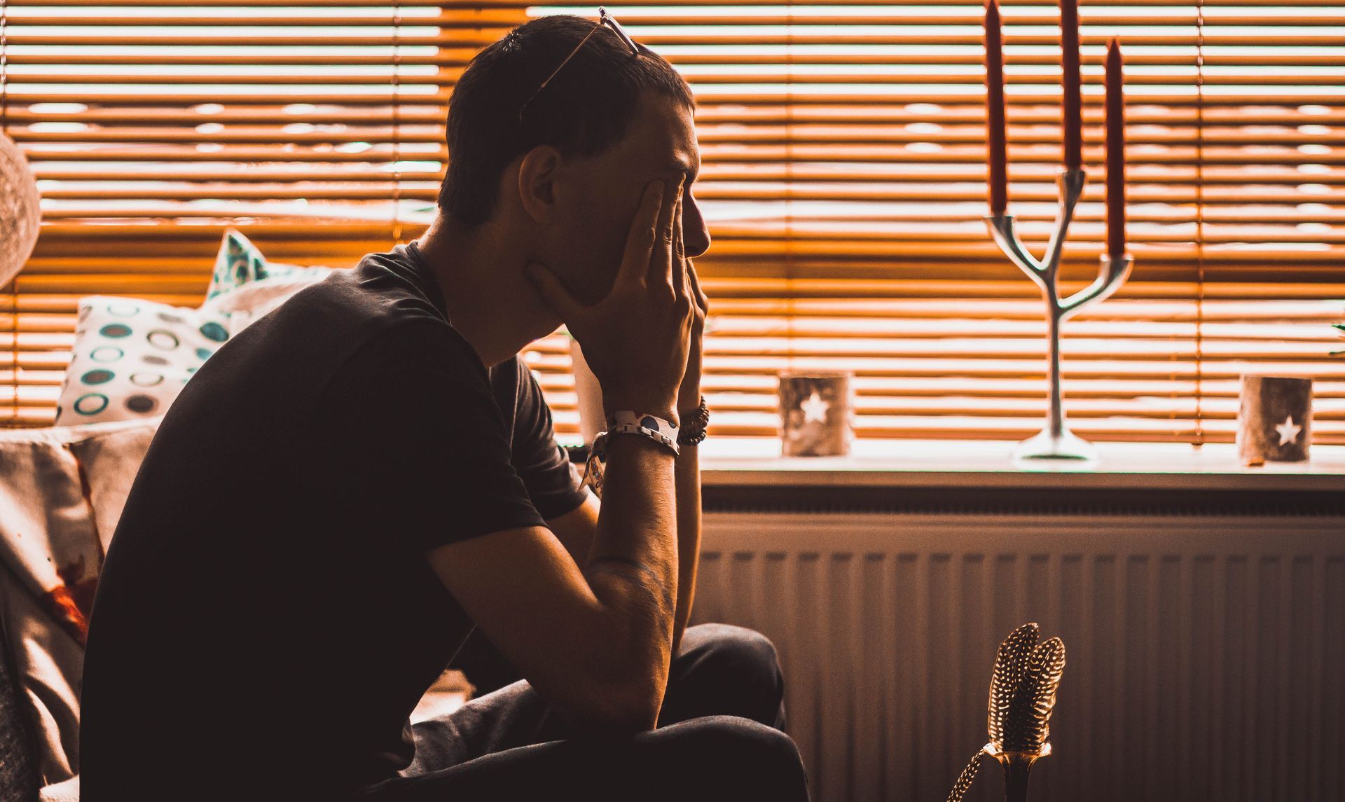 depressed man sitting in front of a window covering his face