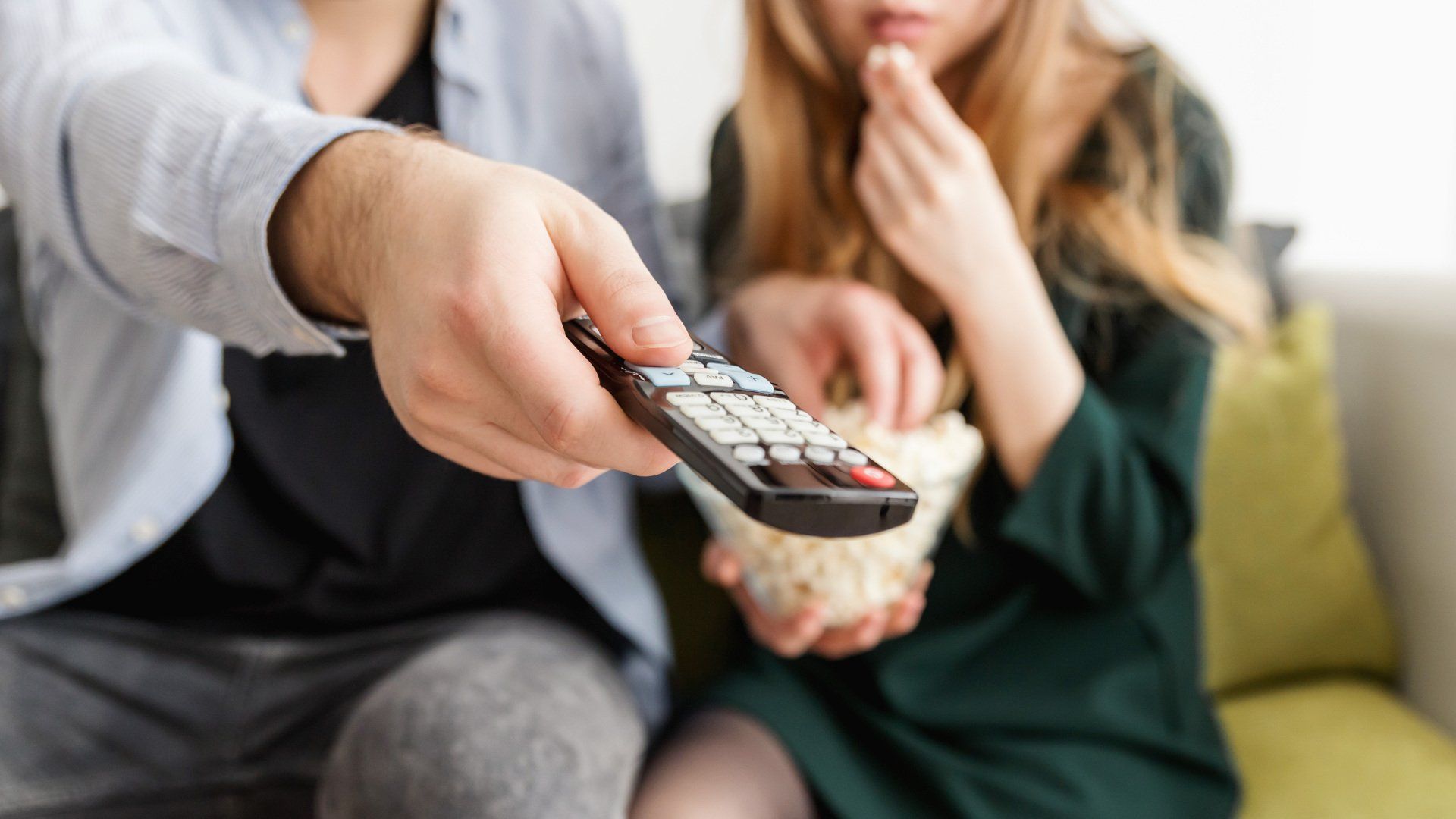 Man holding a remote control next to a woman eating popcorn.