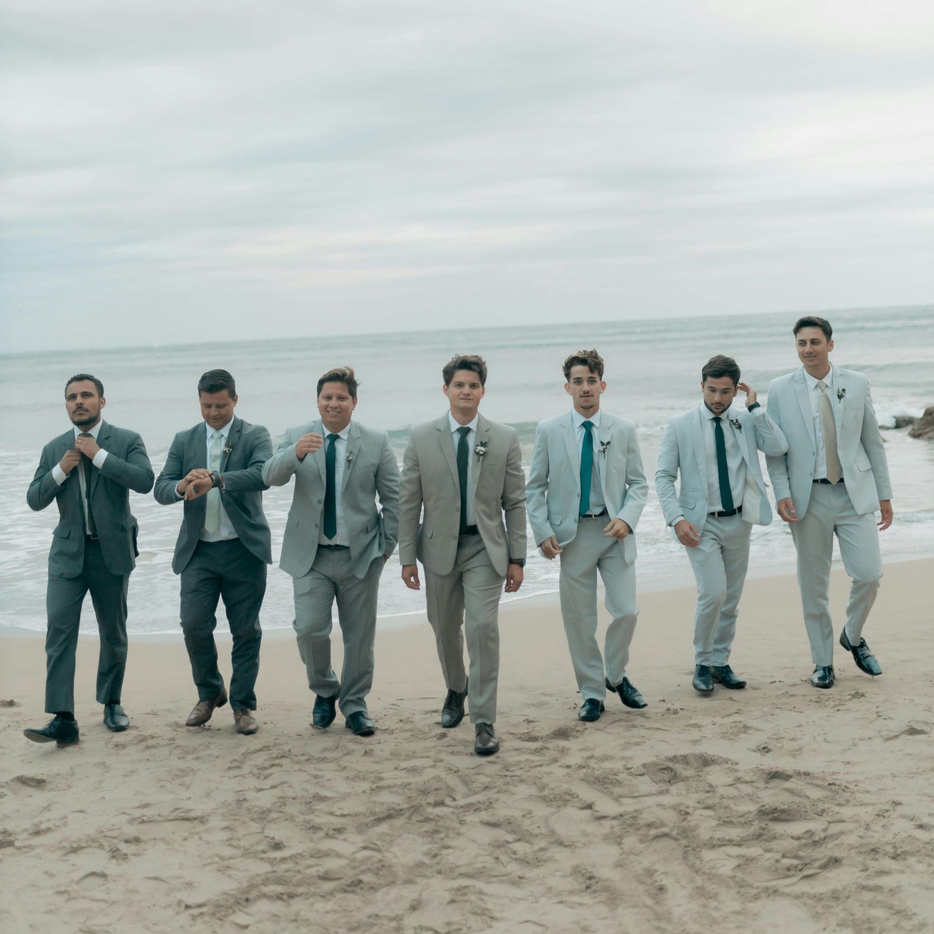A group of men in suits and ties are walking on a beach.