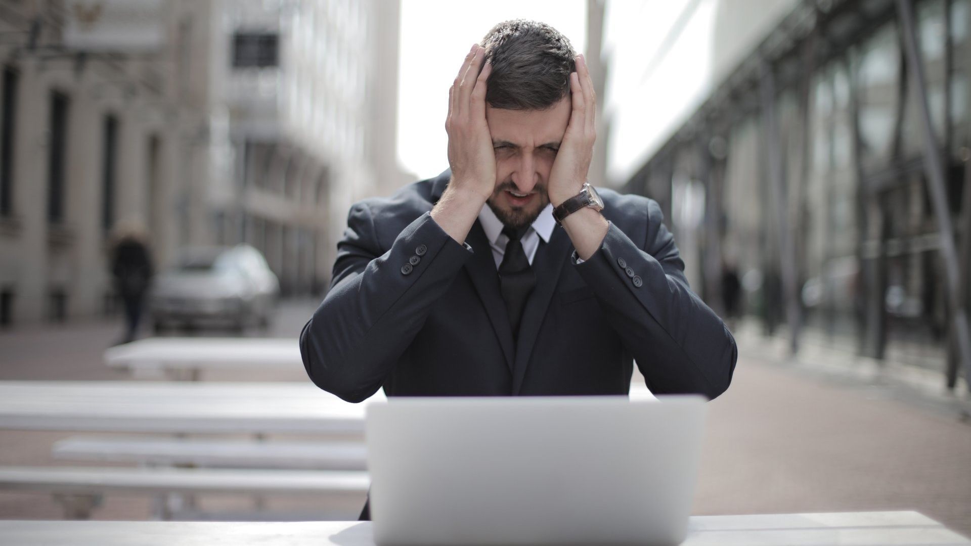 Stressed out man in a suit at a table with his hands on his head in front of a laptop