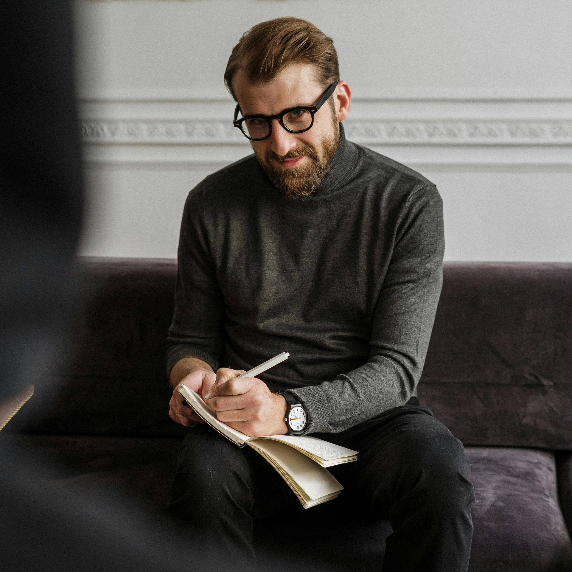A man is sitting on a couch writing in a notebook.