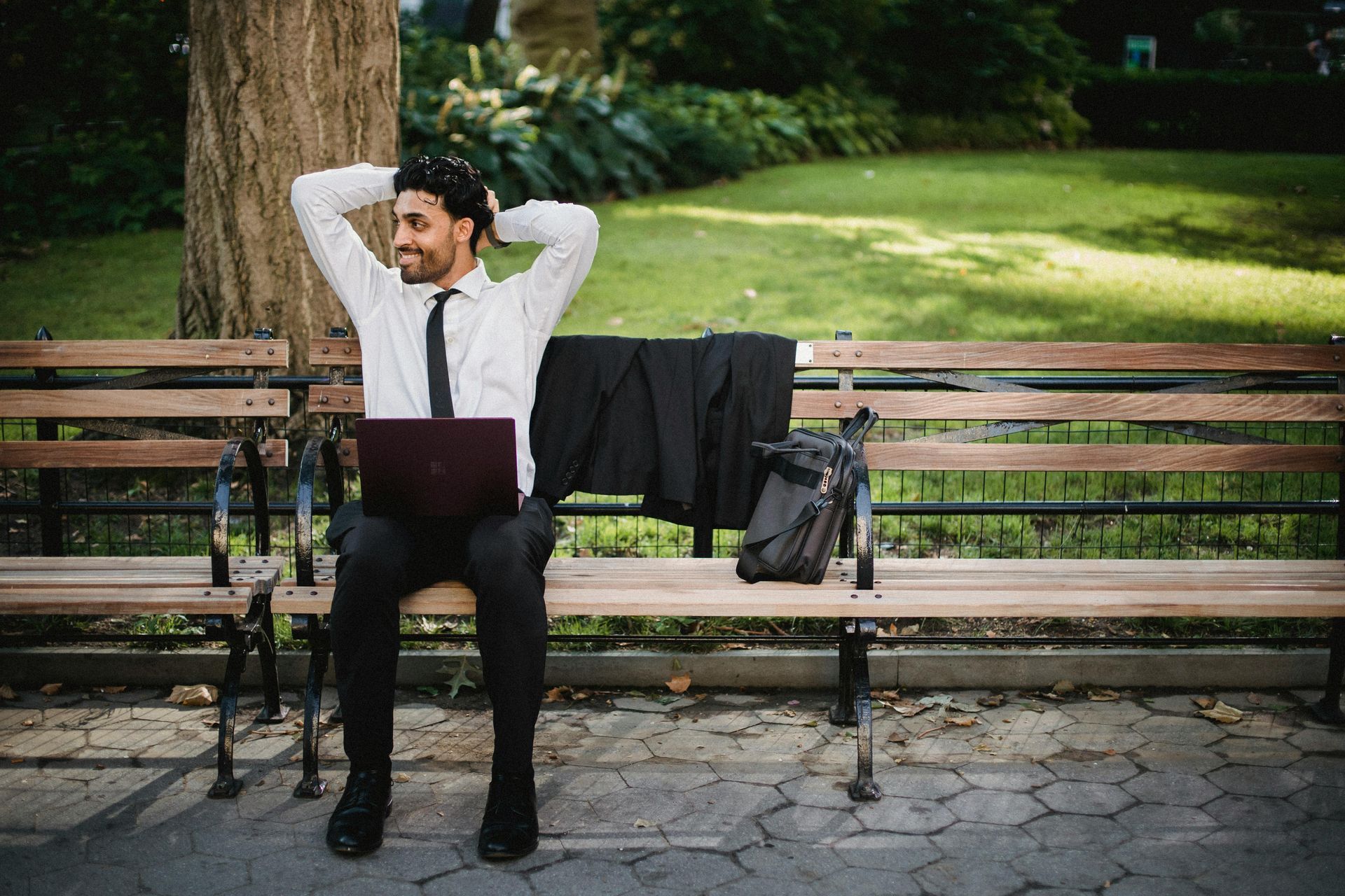 A man is sitting on a park bench with a laptop.