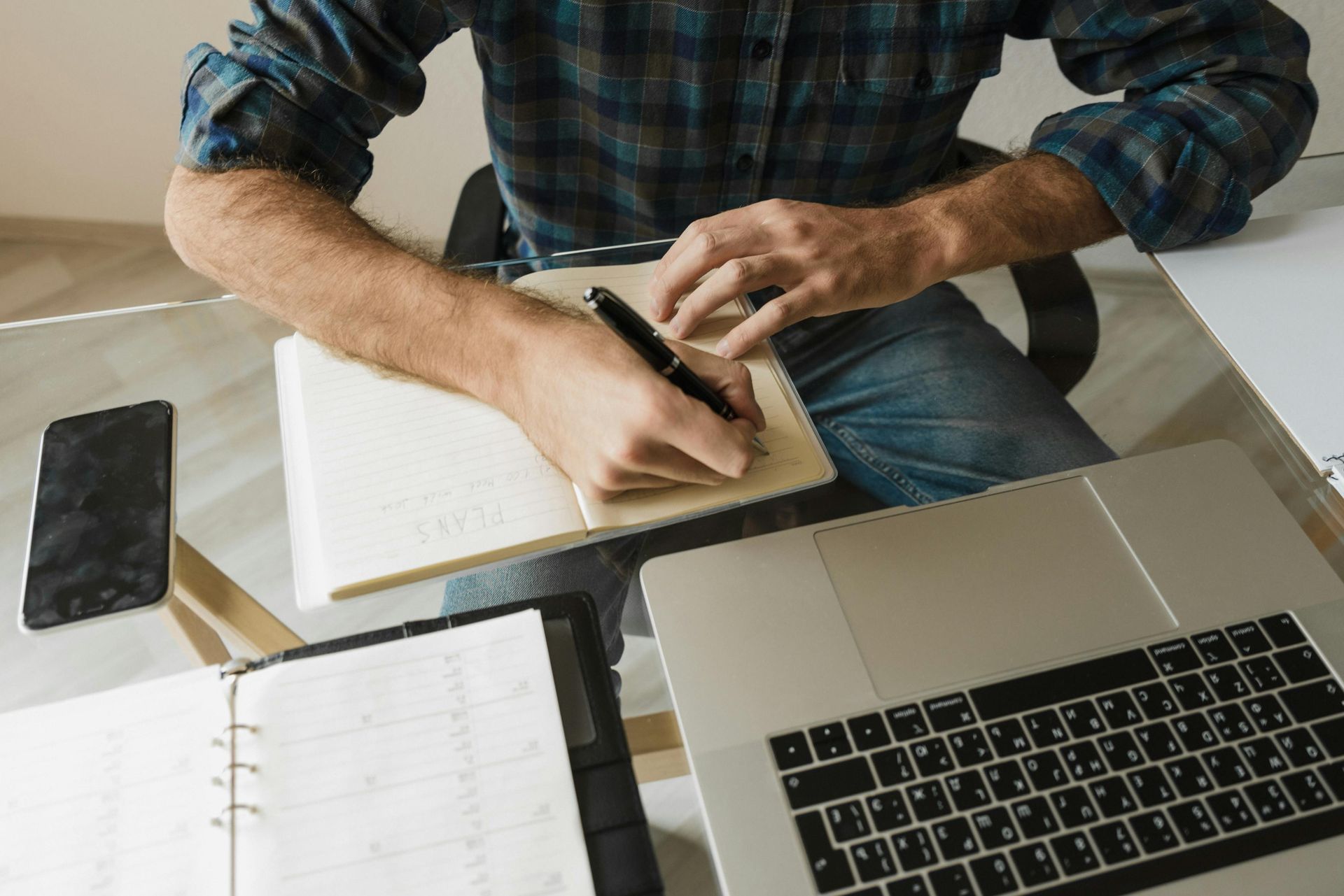 A man is sitting at a desk with a laptop and a notebook.