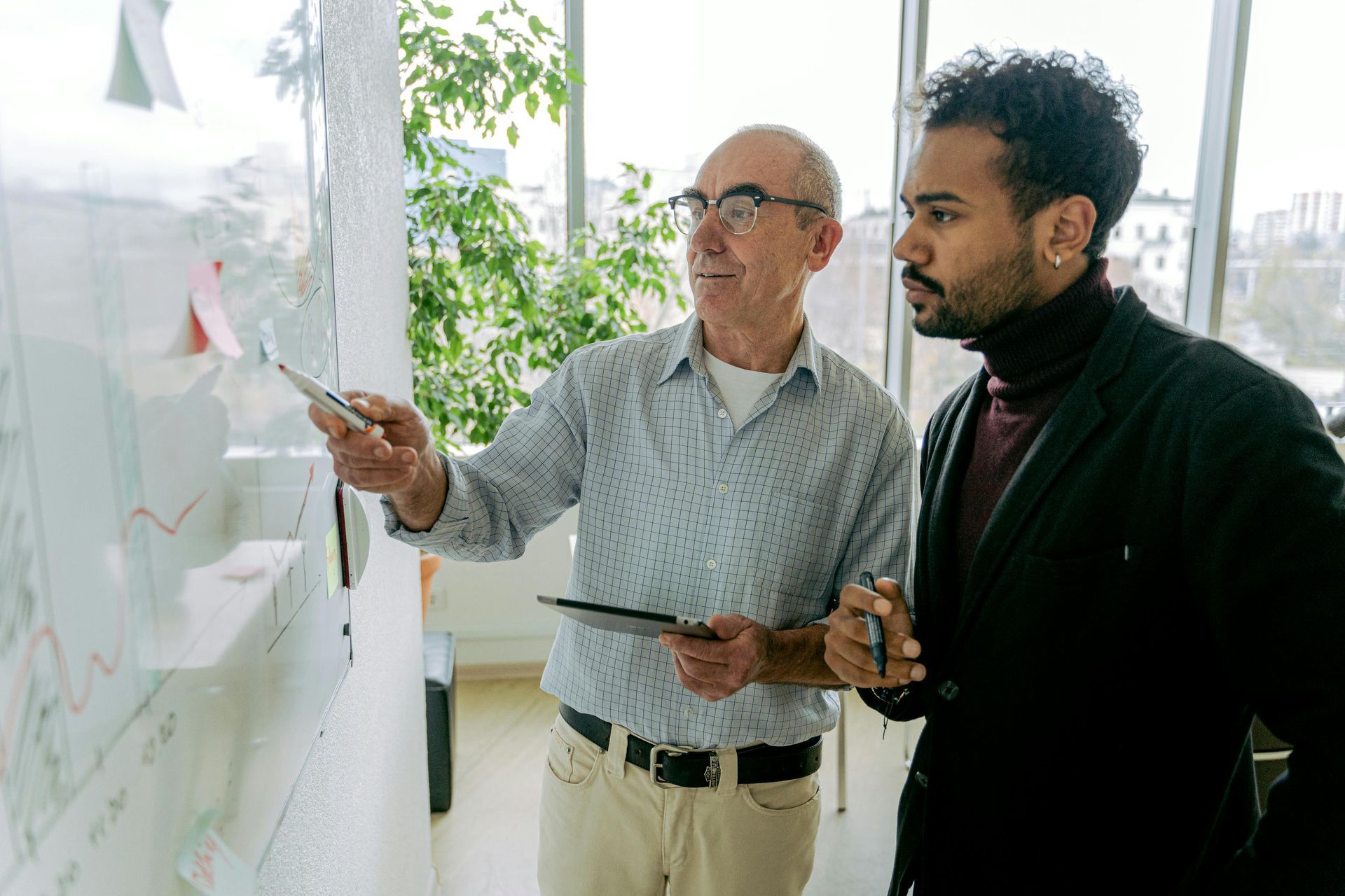Two men are standing next to each other looking at a whiteboard.
