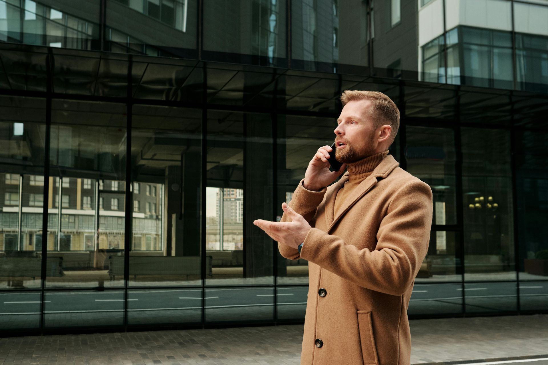 A man in a coat is talking on a cell phone in front of a building.