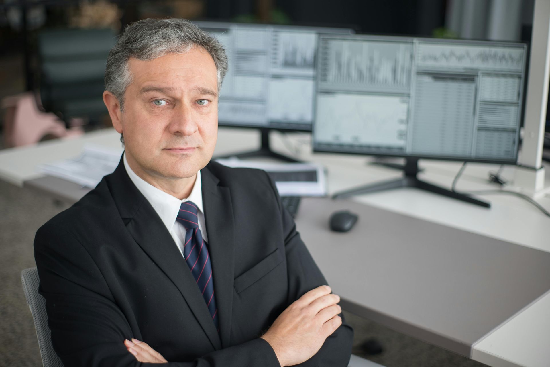 A man in a suit and tie is sitting at a desk with his arms crossed.
