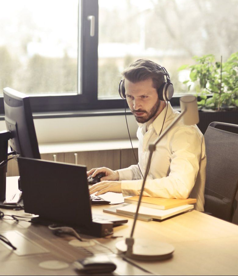 A man wearing headphones is sitting at a desk in front of a computer.