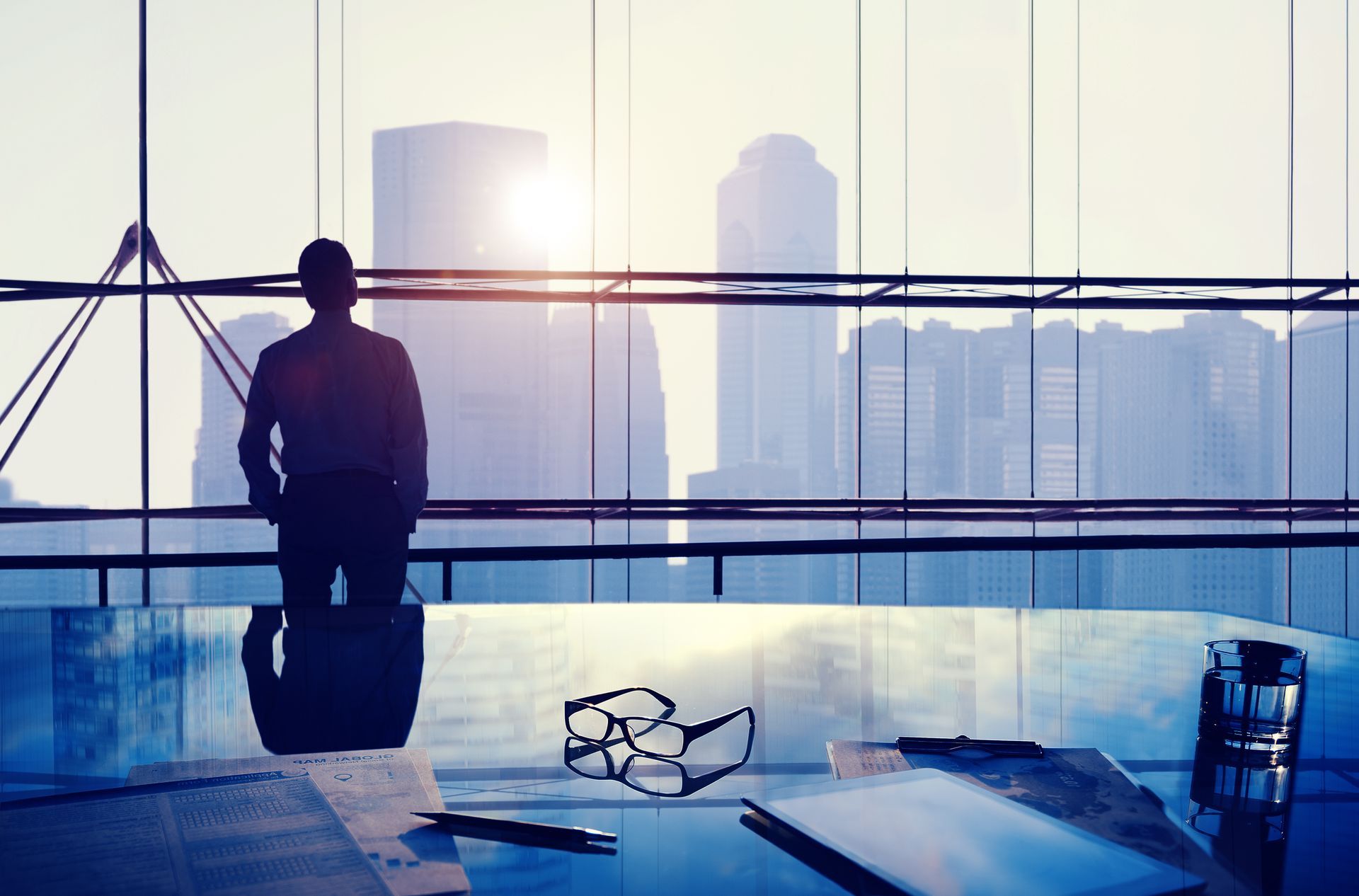 Silhouette of a man in an office looking out at a cityscape with the sun shining.