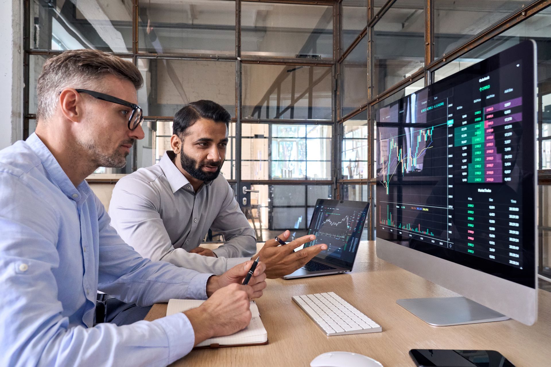 Two men are sitting at a table looking at a computer screen.