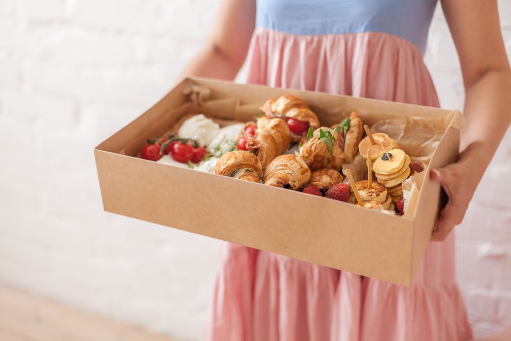 A Woman in a Pink Dress is Holding a Box of Food — Mumbo's Pizza'n'Pasta In Lismore, NSW