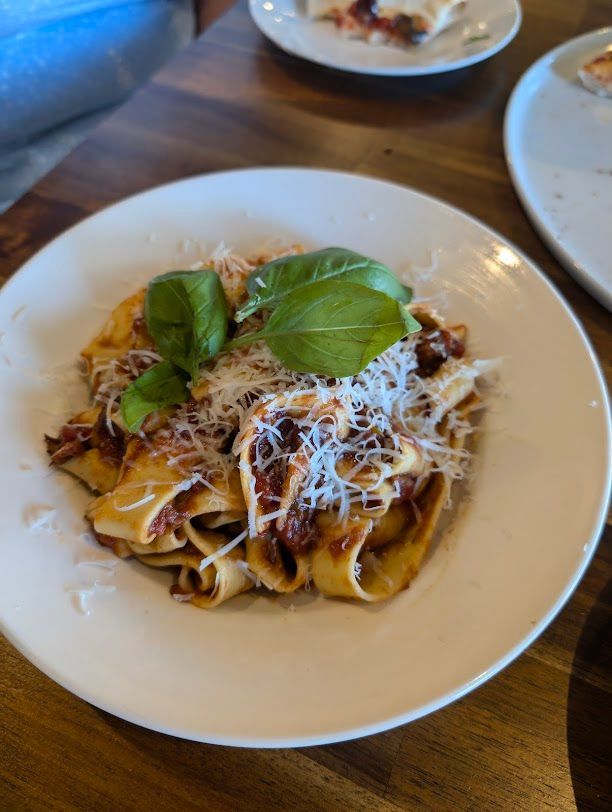 A White Plate Topped With Pasta And Basil On A Wooden Table — Mumbo's Pizza'n'Pasta In Lismore, NSW
