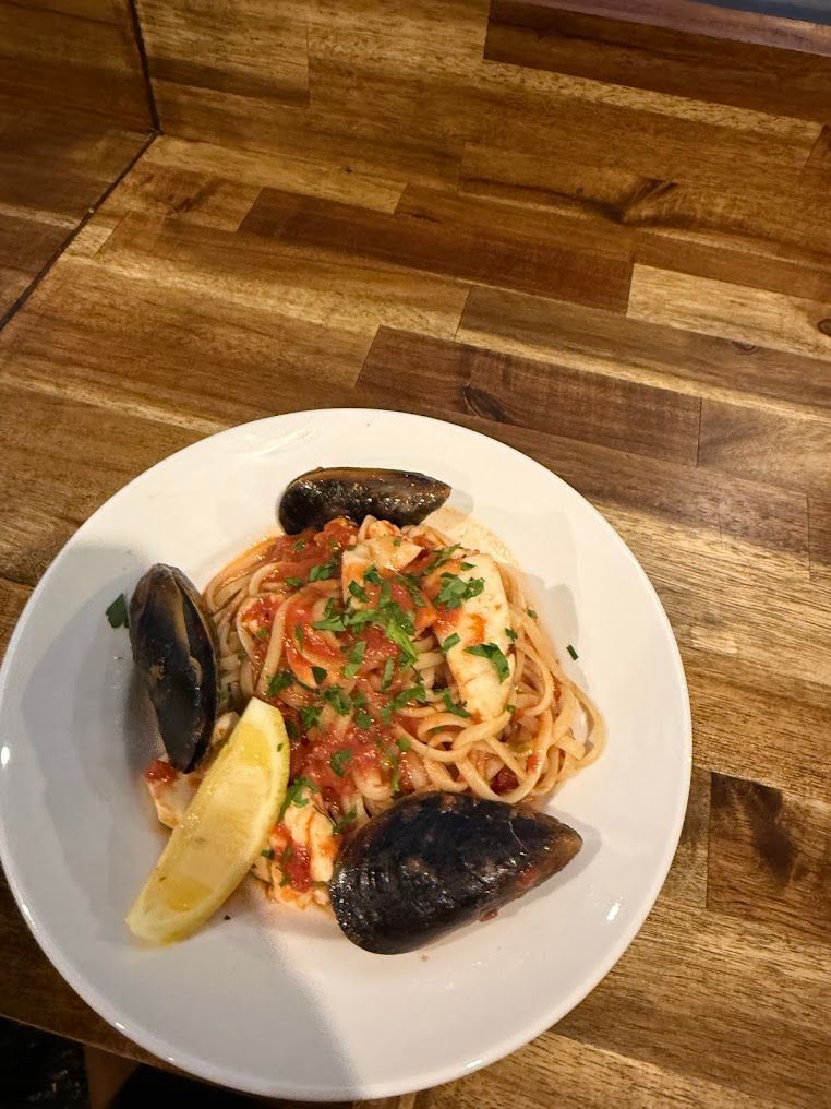 A White Plate Topped With Spaghetti And Mussels On A Wooden Table — Mumbo's Pizza'n'Pasta In Lismore, NSW
