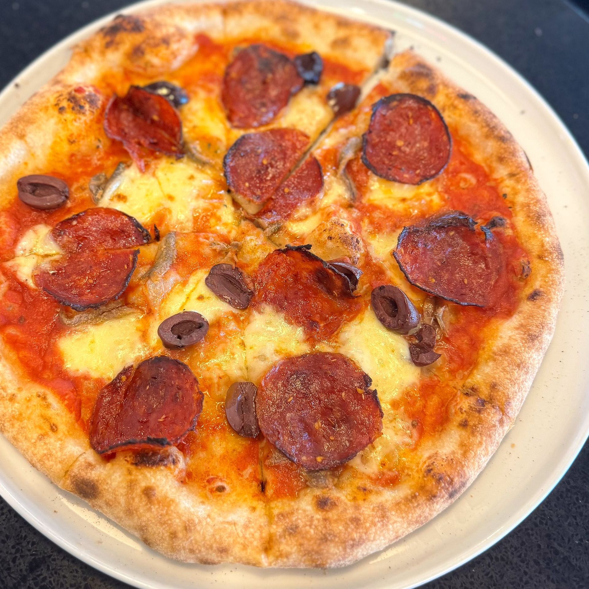 A pizza with pepperoni and olives on a white plate.