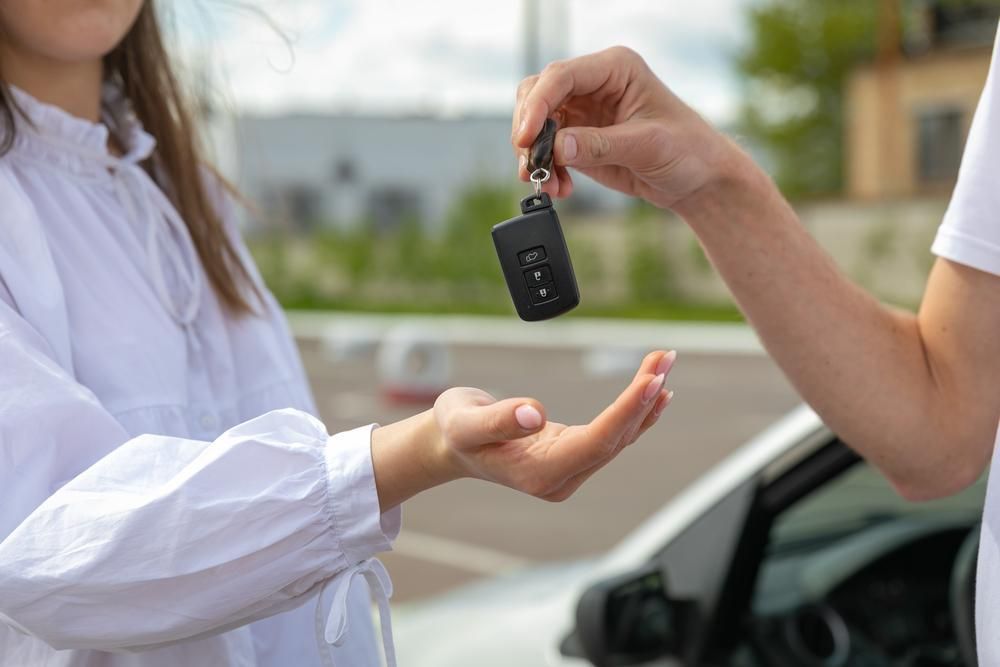 A Man Is Handing A Car Key To A Woman — Primera Driving School Darwin In Anula, NT