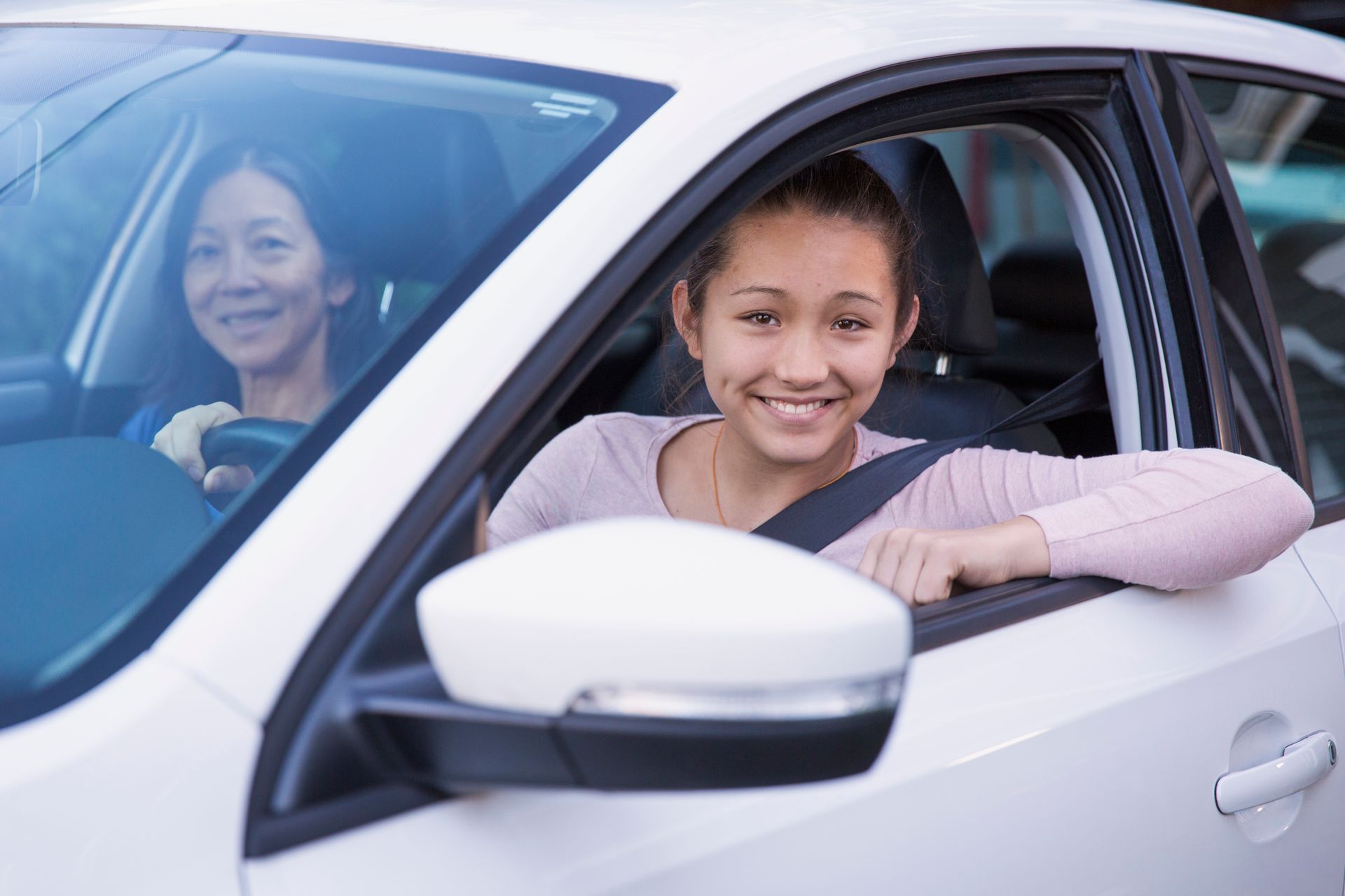 Person driving a white car with a passenger during a safe driving lesson.