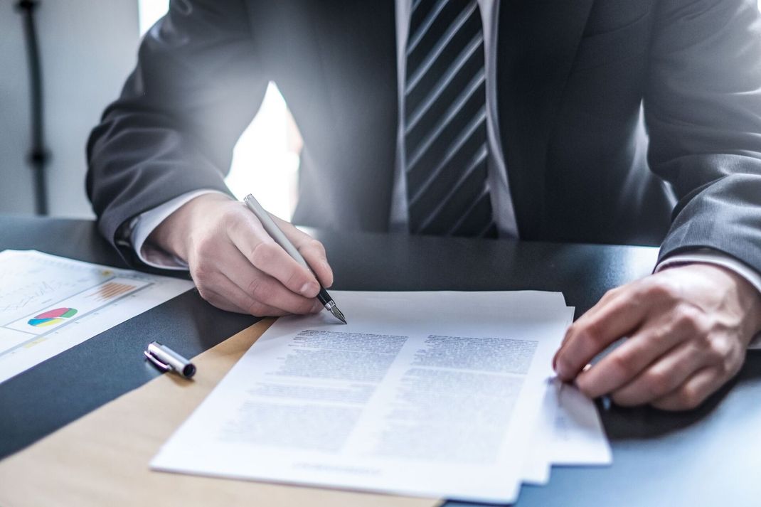 Un uomo in giacca e cravatta sta firmando un documento con una penna.