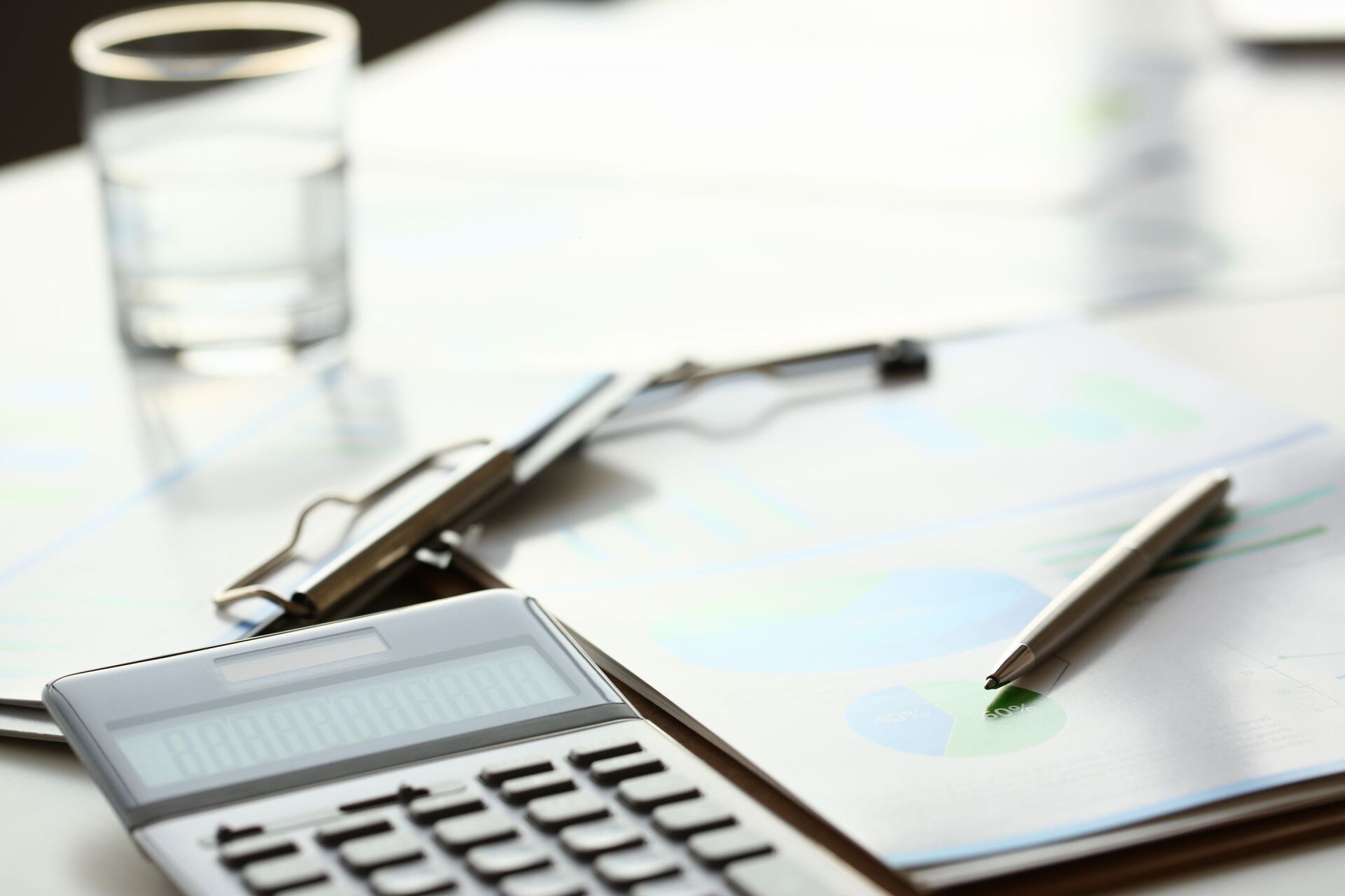 Una calcolatrice è appoggiata su un blocco per appunti, accanto a una penna e degli occhiali.