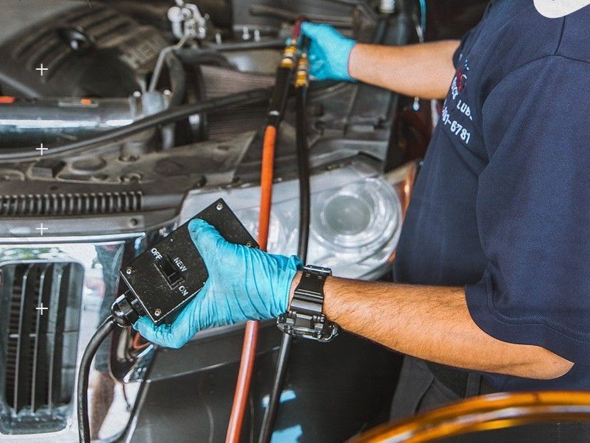 Mechanic in blue gloves connecting equipment to a vehicle's engine, possibly for diagnostics or repair.