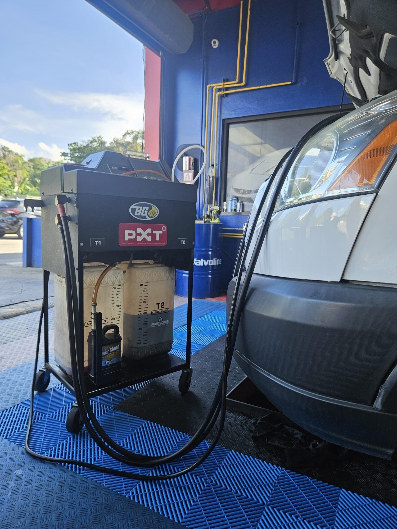 A white car being serviced by a machine with tanks and hoses at a car wash.