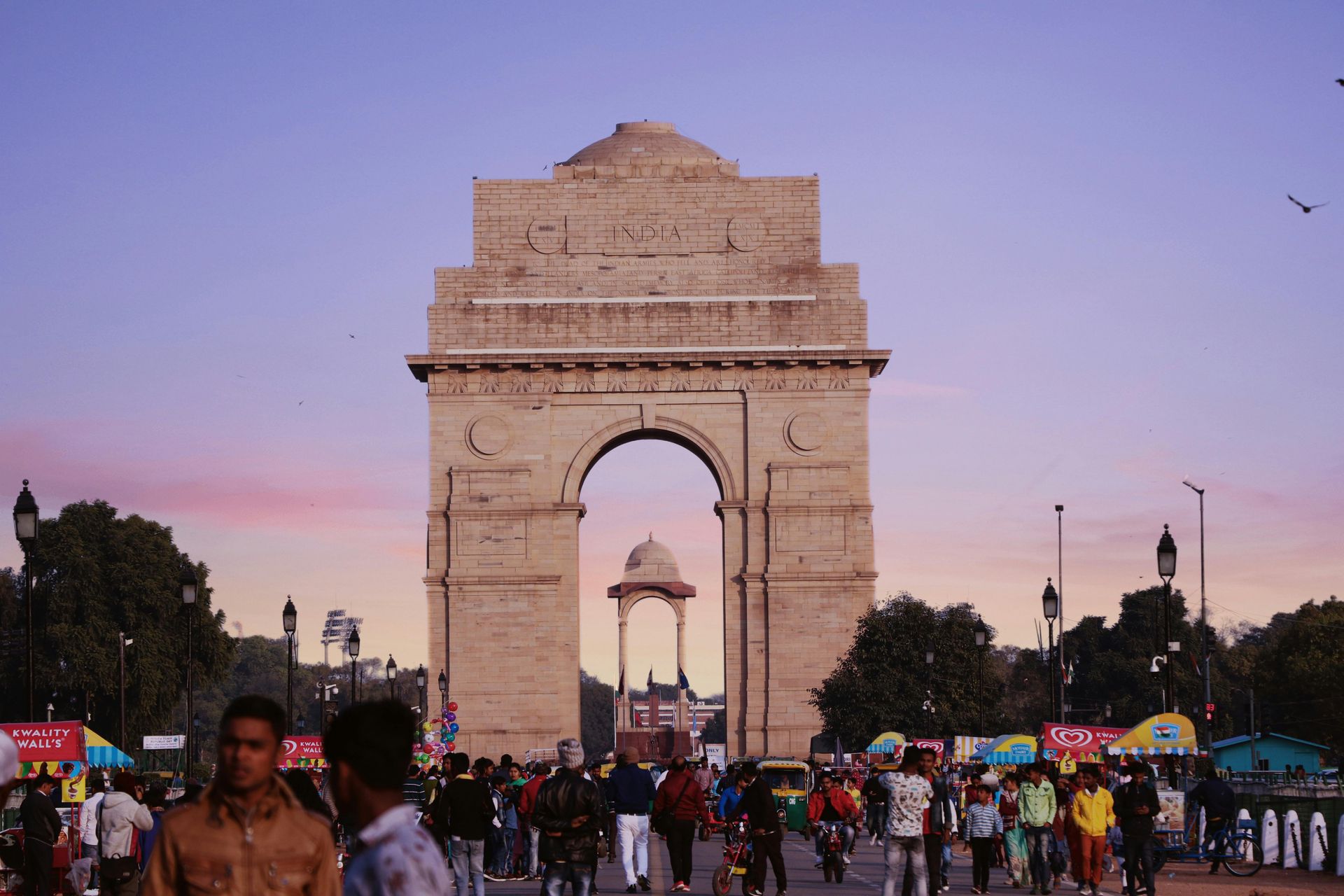 India Gate in Delhi, with people walking and a sunset sky.