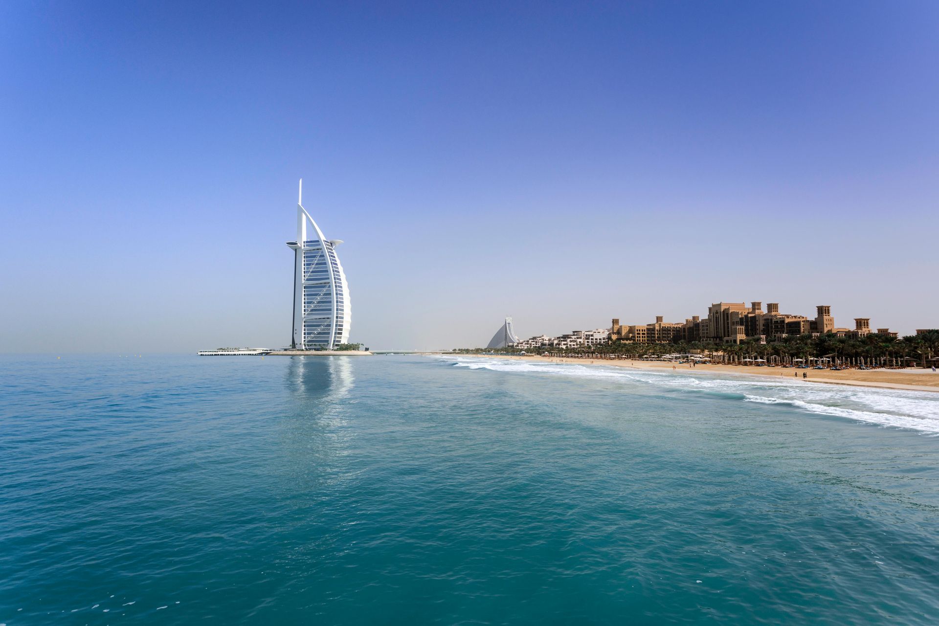 A large building is reflected in the water near a beach Burj Al Arab Dubai